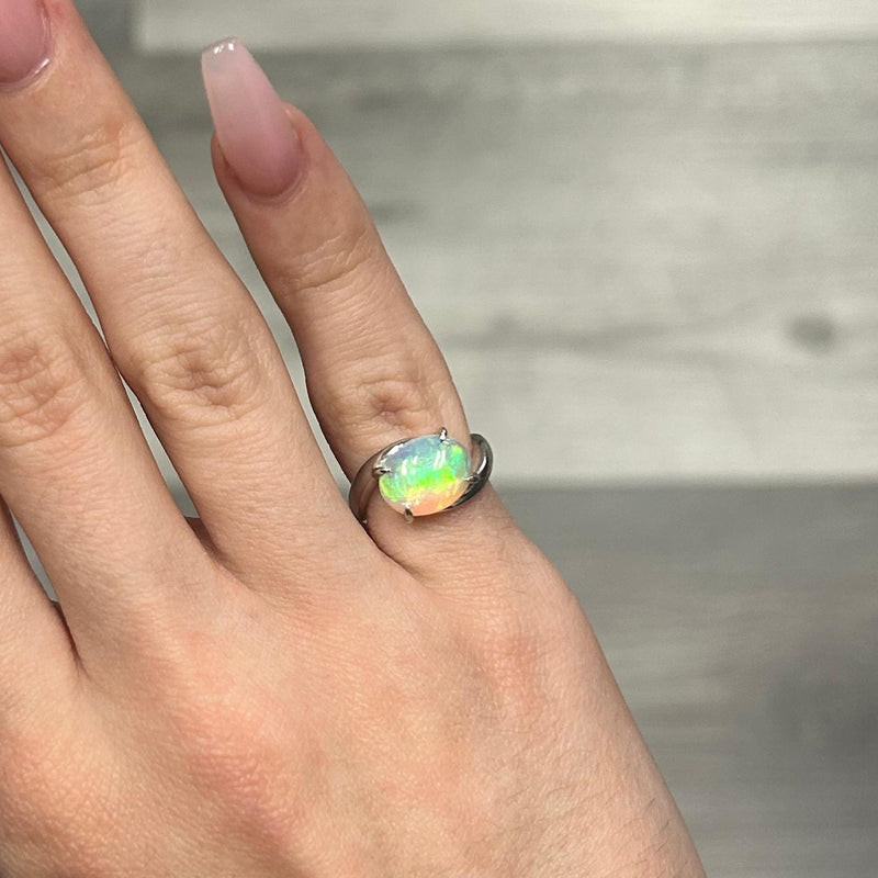 Silver pinky ring with oval opal gemstone and bypass band design.