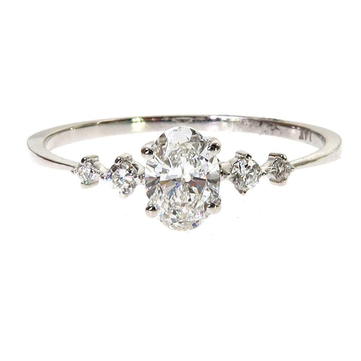 White gold oval diamond ring with six surrounding smaller diamonds on slender band.