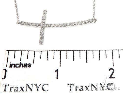 White gold prong-set diamond cross pendant on a delicate chain with ruler for size reference