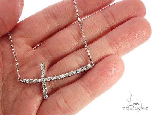 White gold prong-set diamond cross pendant on delicate chain, held in hand for scale