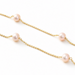 Gold chain necklace with evenly spaced soft pink pearls on a white background.