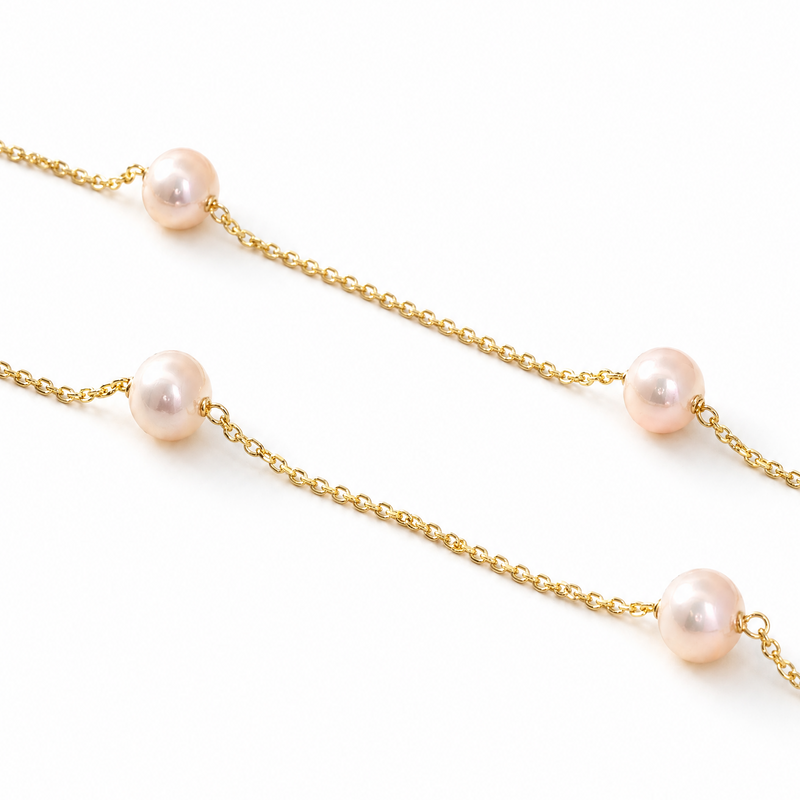 Gold chain necklace with evenly spaced soft pink pearls on a white background.