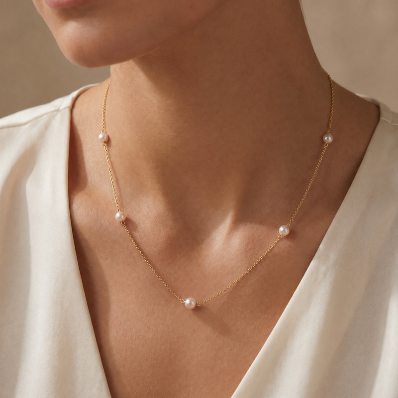 Delicate gold chain necklace with evenly spaced small round white pearls on neck.