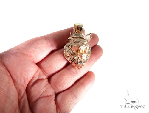Small yellow gold lion head pendant encrusted with diamonds, held in hand for scale