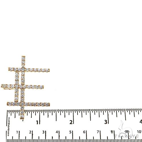 Yellow gold triple cross pendant encrusted with round diamonds, beside a ruler for size reference