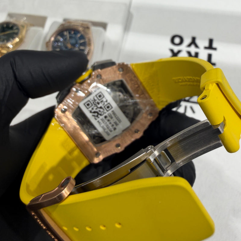 Rose gold Richard Mille RM 11-03 watch with skeleton dial and vibrant yellow rubber strap.