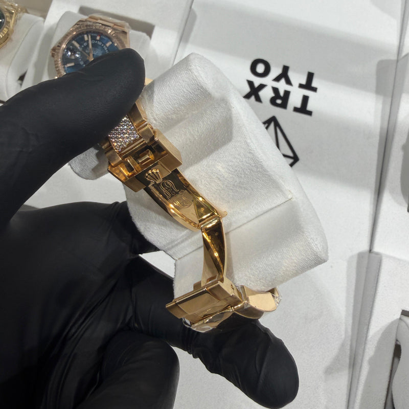 Gold-tone metal watch bracelet with folding clasp held by gloved hand.