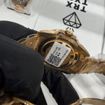 Gold-tone wristwatch with black dial and translucent protective case held by gloved hand.