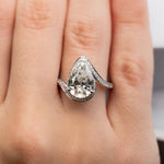 Pear-shaped diamond engagement ring with pavé diamond band in white gold.