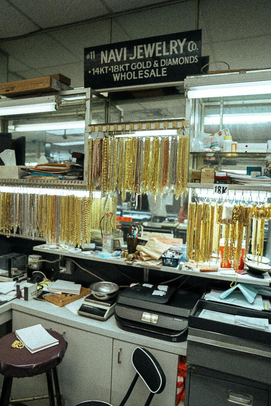 The Navi Jewelry Co. booth sign above racks of hanging gold chains