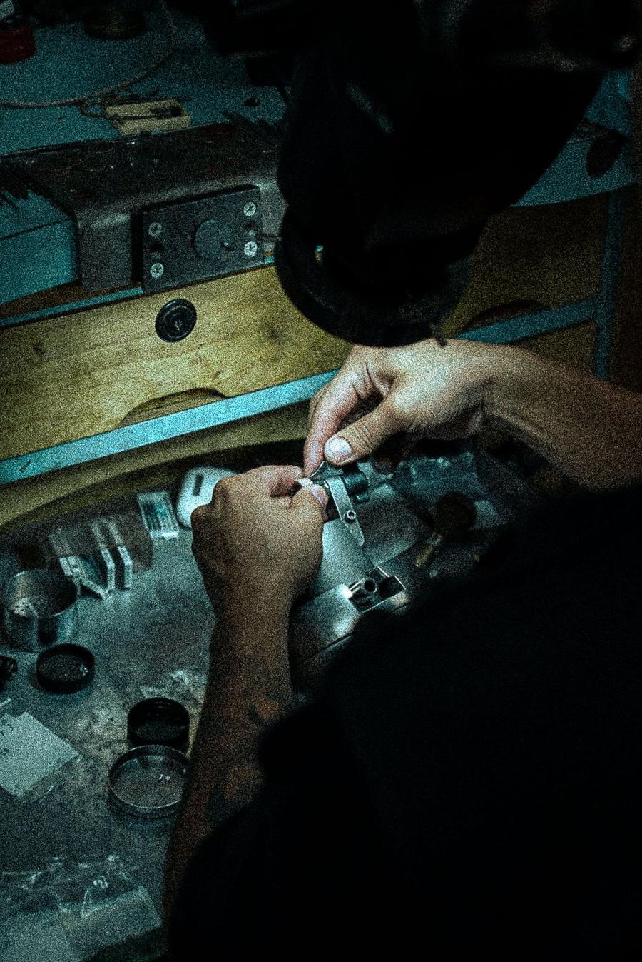 Hands at a jeweler's bench working a piece held in a setting clamp
